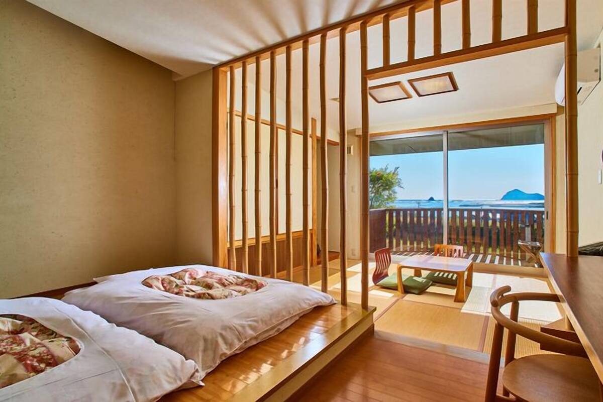 A room with a bed, a table, and a view of the ocean.