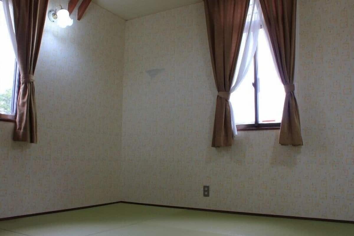 A room with patterned wallpaper, two windows with curtains, a light fixture, and a tiled floor.