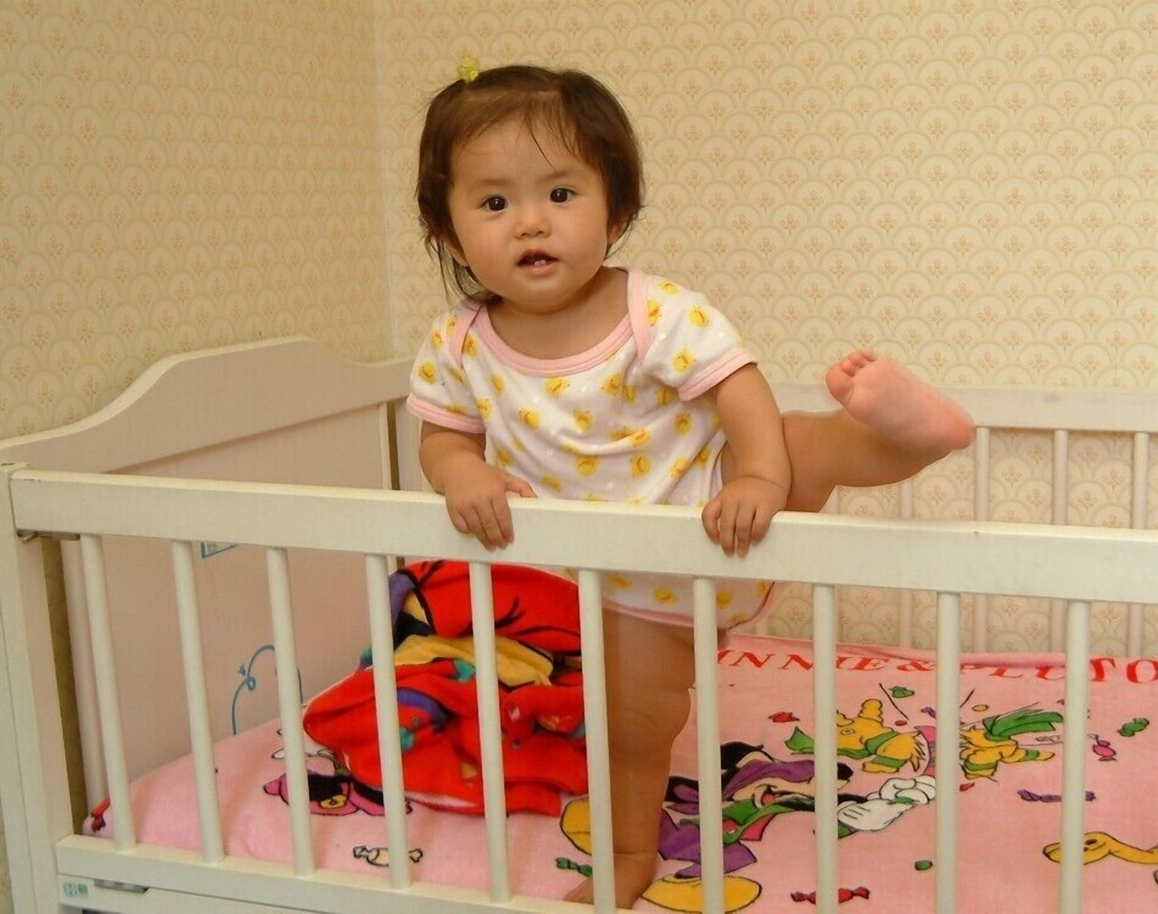 A child in a crib with a patterned wall in the background.