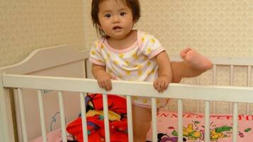 A child in a crib with a patterned wall in the background.