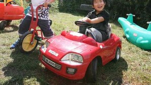 Two children playing with toy cars in a grassy outdoor area with a house in the background. - Kids Pension Fruit Juice Awajishima (Awaji)