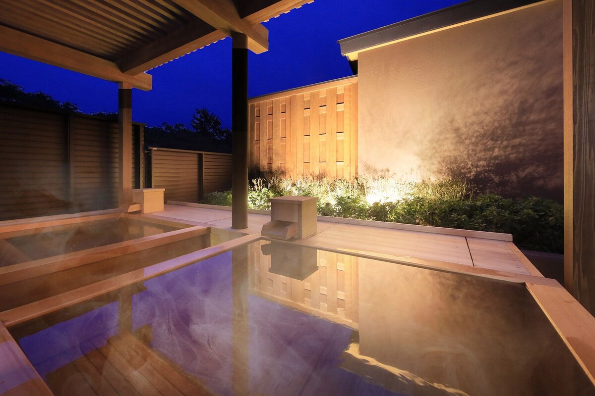 Un espace moderne pour bains à remous en plein air, doté d’une terrasse en bois et d’une enceinte en verre.