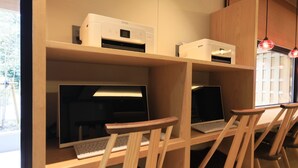 Ein Arbeitsbereich mit zwei Schreibtischen, jeweils ausgestattet mit einem Computer und einer Tastatur, und einem Drucker an der Wand.