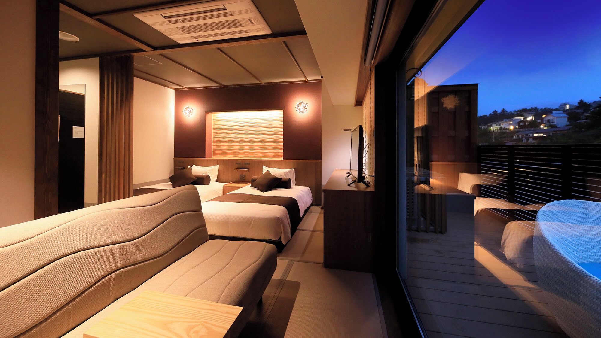 A modern hotel room with a balcony, a bed with multiple pillows, a bedside table, and a large window.