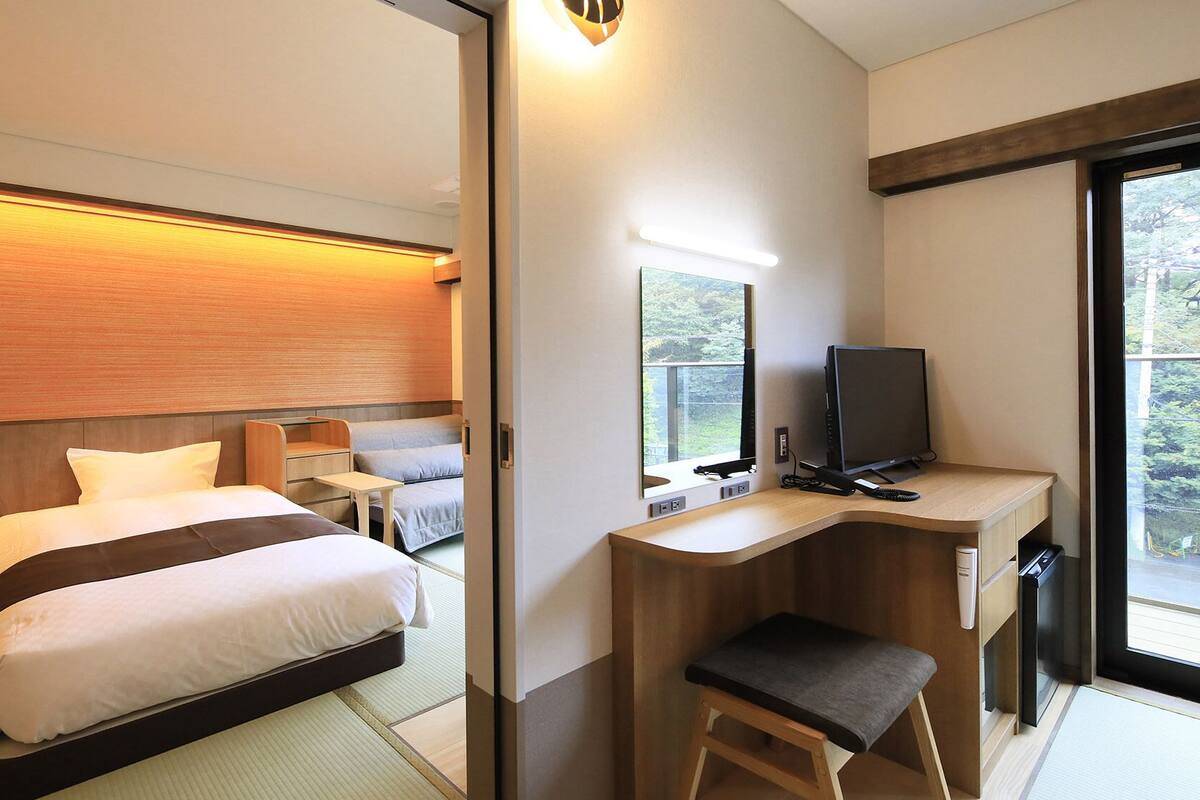 Une chambre d’hôtel équipée d’un lit, d’un bureau, d’une chaise, d’une télévision et d’une fenêtre donnant sur un paysage agréable.