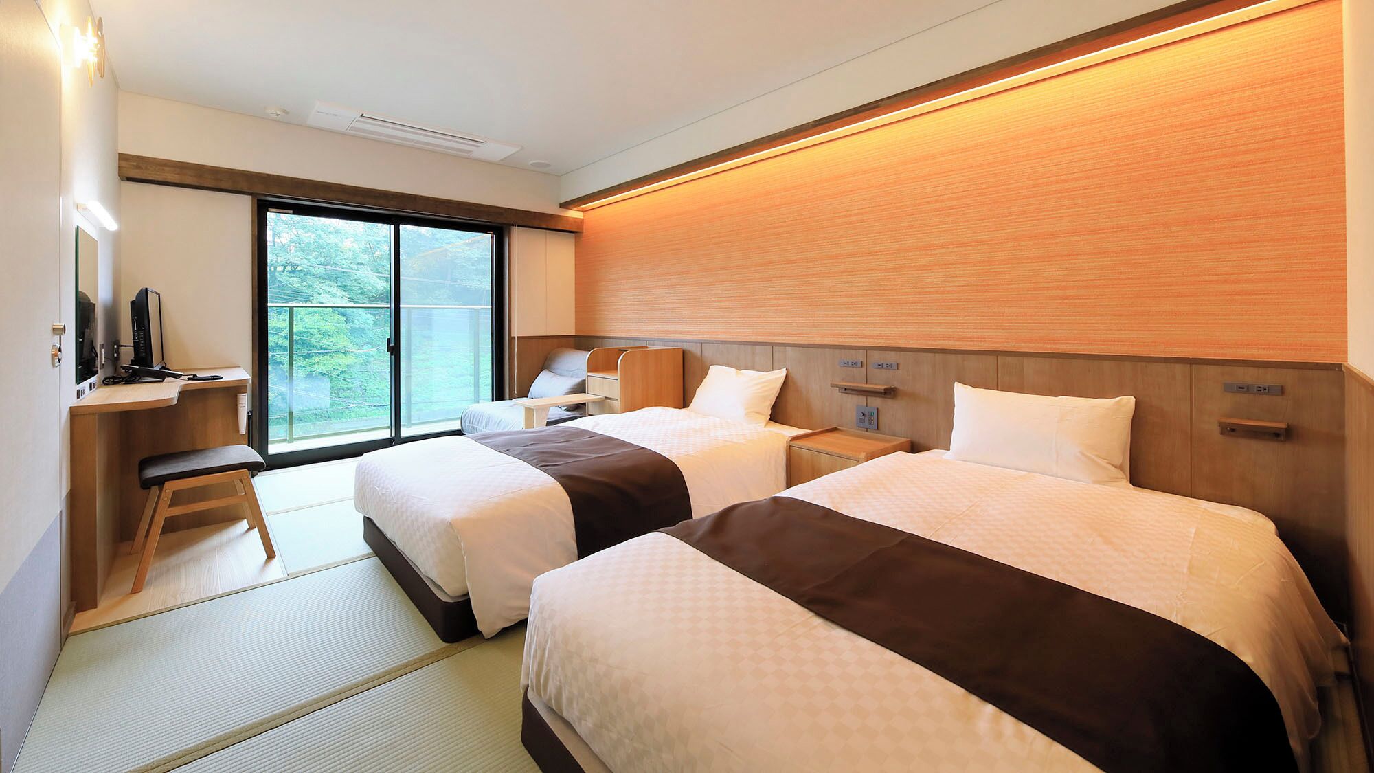 A hotel room with two beds, a desk with a computer, a chair, a TV, and a sliding glass door to the outside.