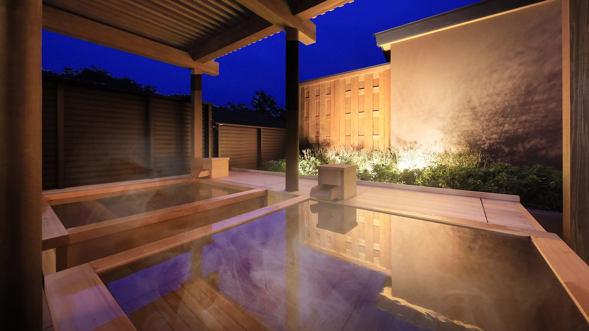 A modern outdoor hot tub area with wooden decking and a glass enclosure.