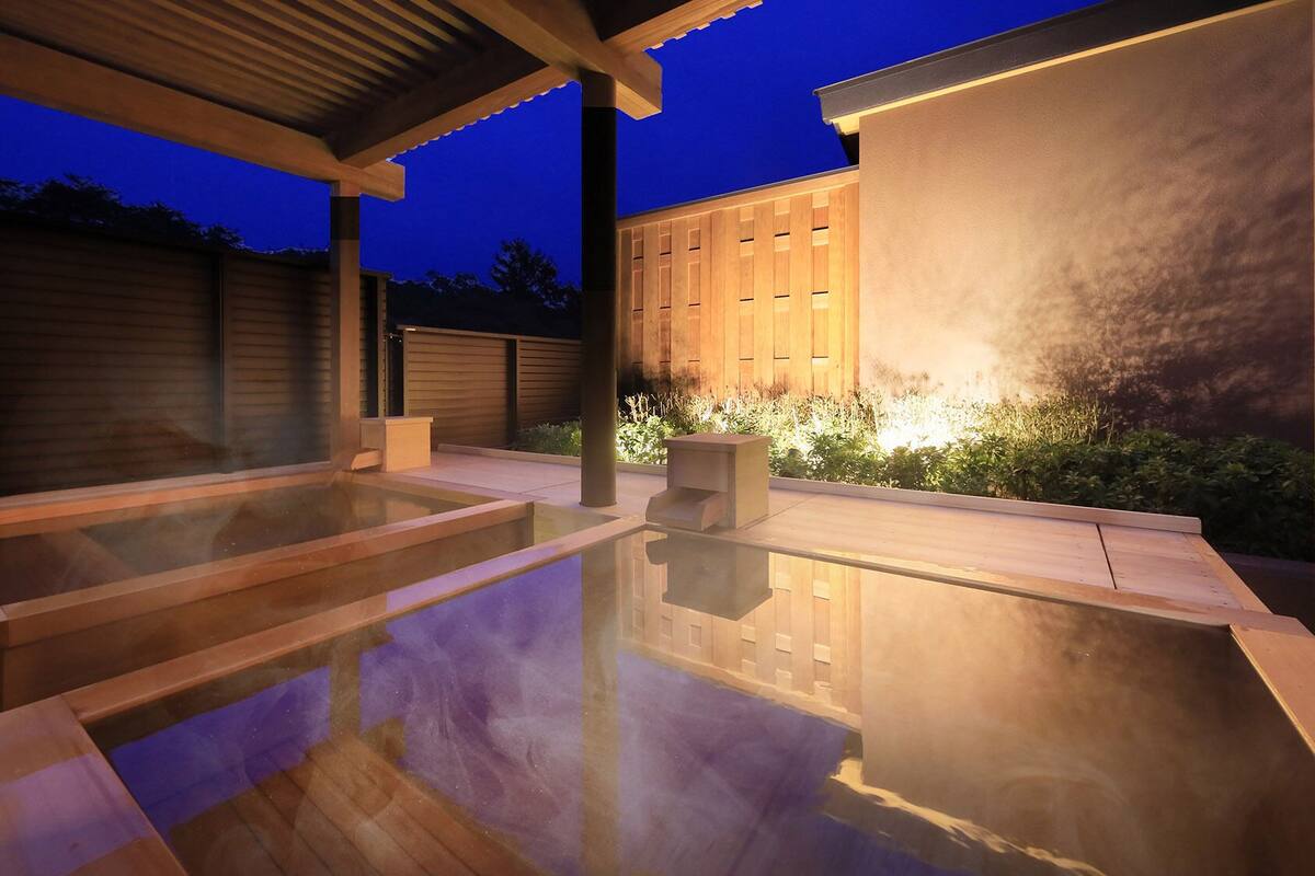 Un espace moderne pour bains à remous en plein air, doté d’une terrasse en bois et d’une enceinte en verre.