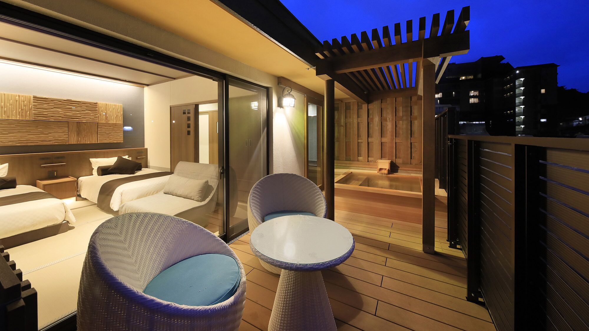 A modern hotel room with a balcony, a jacuzzi, and a seating area with two chairs and a table.