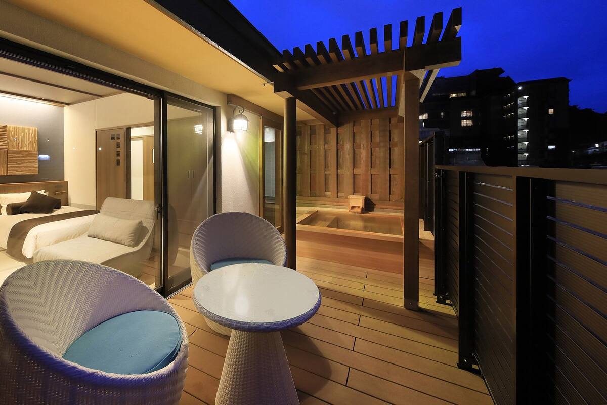 Une chambre d’hôtel moderne dotée d’un balcon, d’un jacuzzi et d’un coin salon avec deux fauteuils et une table.