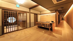 Ein Hotel-Rezeptionsbereich mit einem Holzbüro, einer traditionellen japanischen Schiebetür und einem Hinweisschild für einen Ausgang.