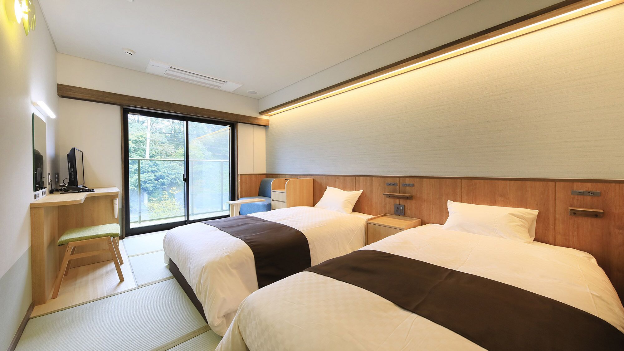A hotel room with two beds, a desk with a computer, a chair, and a large window with a view.
