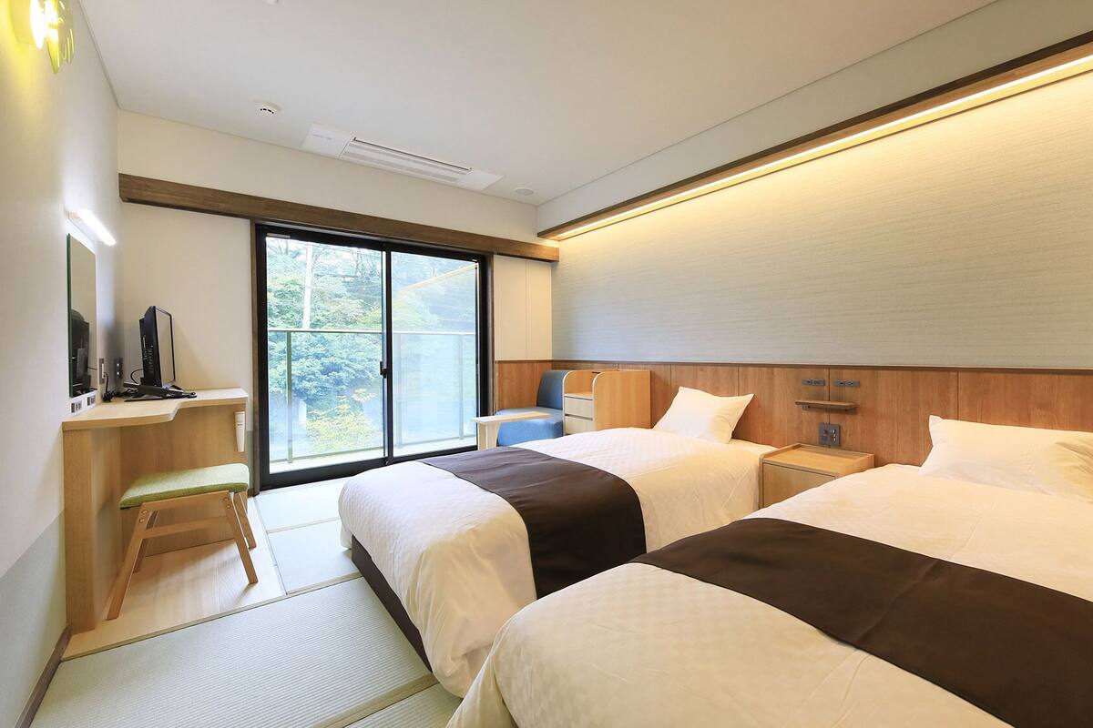 Une chambre d’hôtel avec deux lits, un bureau avec un ordinateur, une chaise et une grande fenêtre donnant sur un beau paysage.