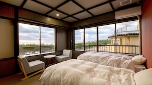 A hotel room with two beds, a small round table, a chair, and large windows offering a view of the city. - Taiheian (Sakai)