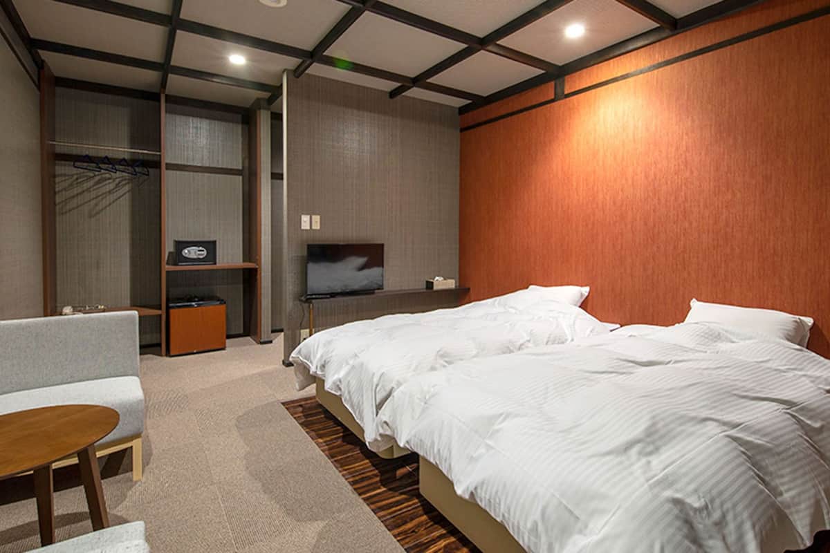 A hotel room with a bed, a TV, a seating area, and a wardrobe.