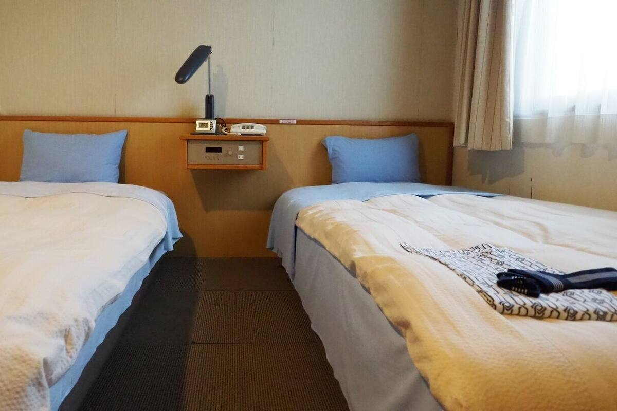 A hotel room with two beds, a nightstand with a radio and clock, and a window with curtains.