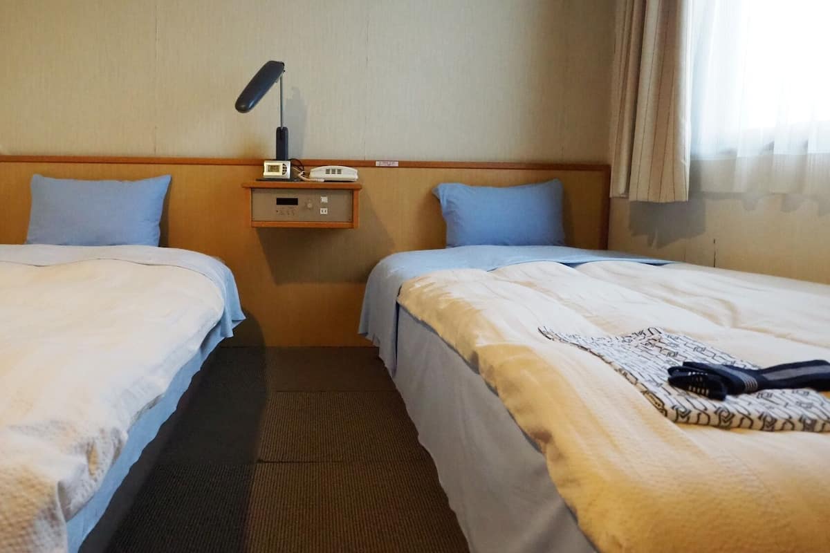 A hotel room with two beds, a nightstand with a lamp and phone, and a carpeted floor.