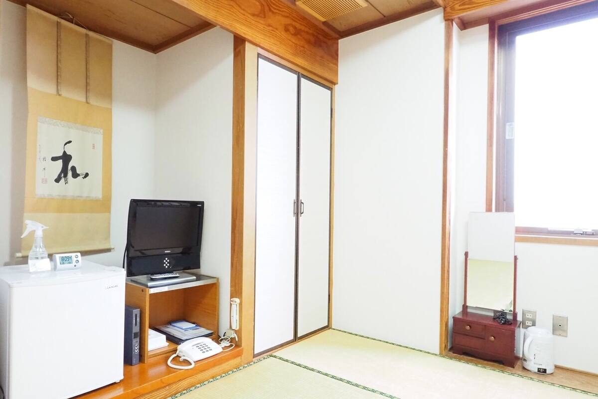 A room with a wooden cabinet, a television, a desk with a phone, a small shelf with books, and a sliding door closet.