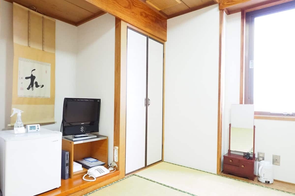 A room with a wooden cabinet, a television, a desk with a phone, a small shelf with books, and a sliding door closet.