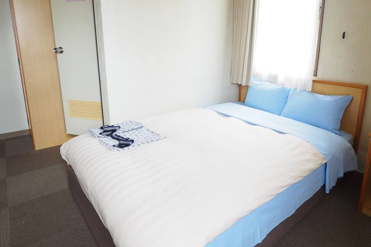 A hotel room with a bed, a nightstand with a lamp, and a window with curtains.