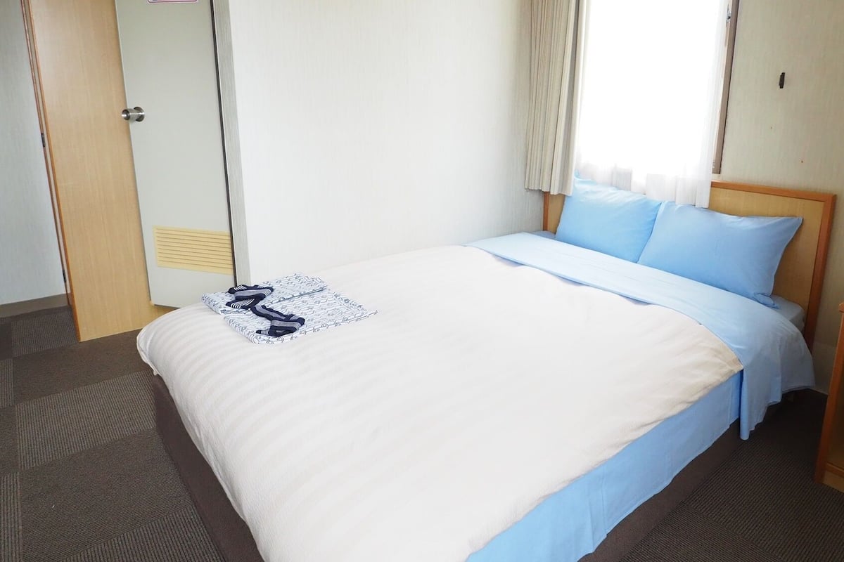 A hotel room with a bed, a nightstand with a lamp, and a window with curtains.