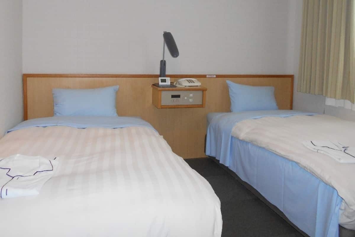 A hotel room with two beds, a nightstand with a phone and a lamp, and a window with curtains.