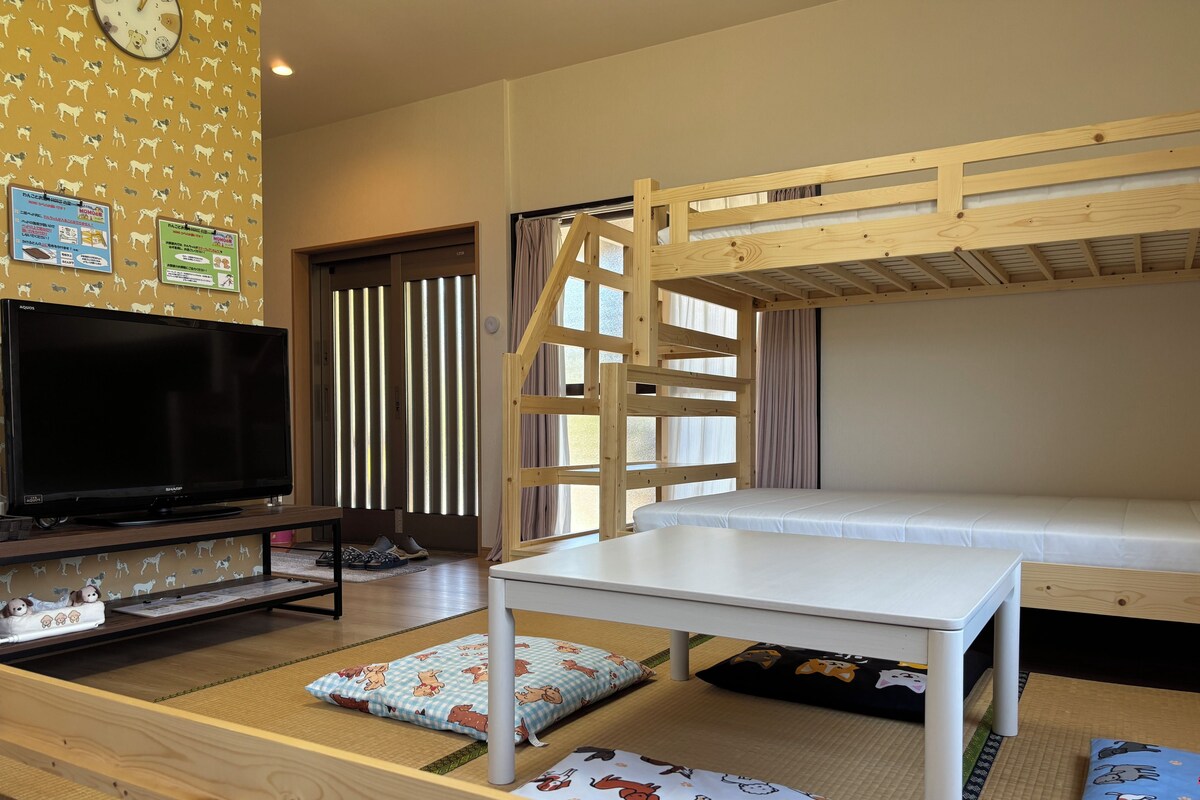 A room with a bunk bed, a television, a table, and a wall clock.