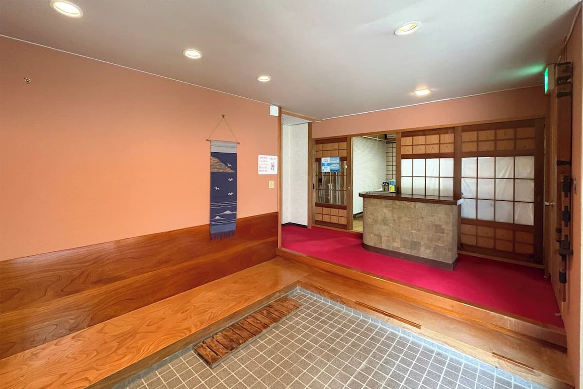 A traditional Japanese-style interior with a reception desk, wooden flooring, and a red carpeted area.