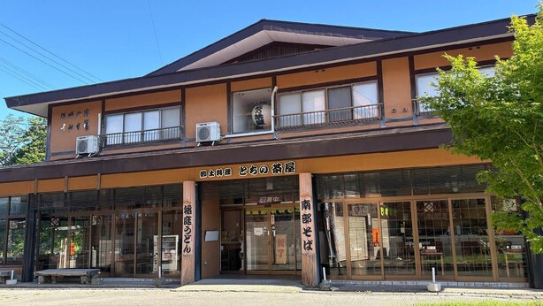 A two-story building with a traditional Japanese architectural style, featuring large glass windows and a wooden entrance.