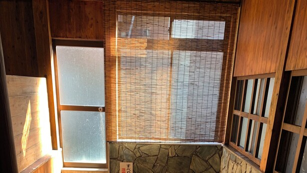A wooden bathhouse with a stone wall, a wooden floor, and a small water feature. - Tsurumisou (Arita)