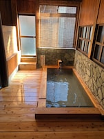 A wooden bathhouse with a stone wall, a wooden floor, and a small water feature.