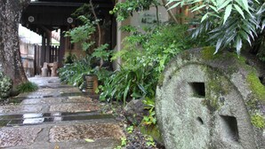 A stone pathway leading to a traditional building with a large stone structure on the right. - Tsurumisou (Arita)
