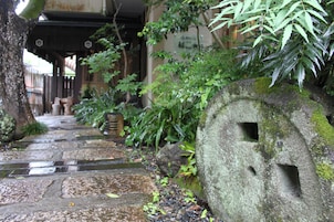 A stone pathway leading to a traditional building with a large stone structure on the right.
