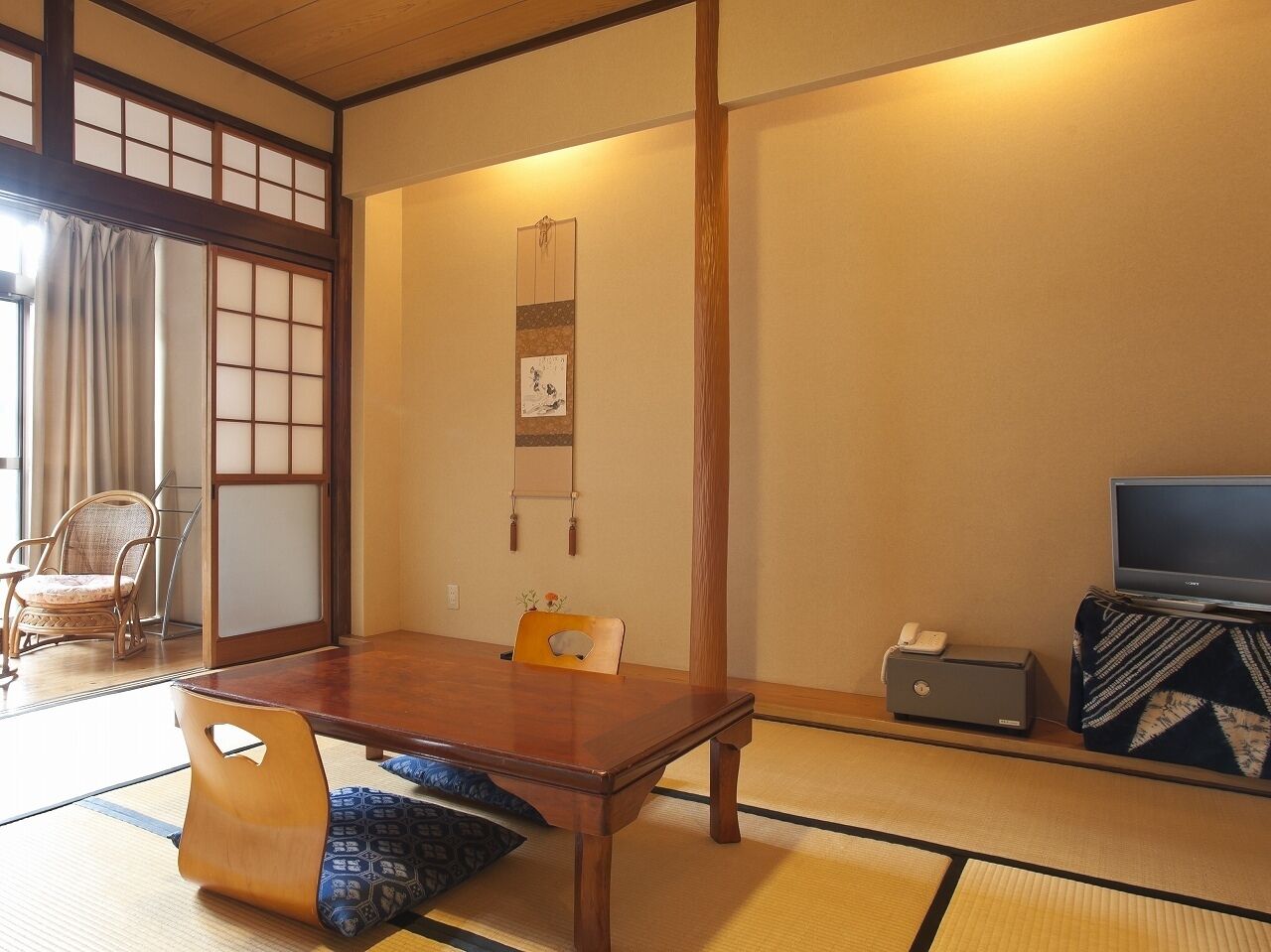 A traditional Japanese room with tatami flooring, a low table, a television, and a desk with a telephone.