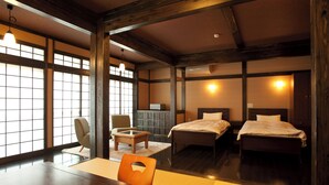 A traditional Japanese-style room with tatami flooring, a low table, a chair, and two beds. - Tsurumisou (Arita)