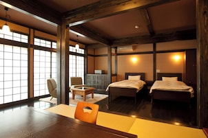 A traditional Japanese-style room with tatami flooring, a low table, a chair, and two beds.