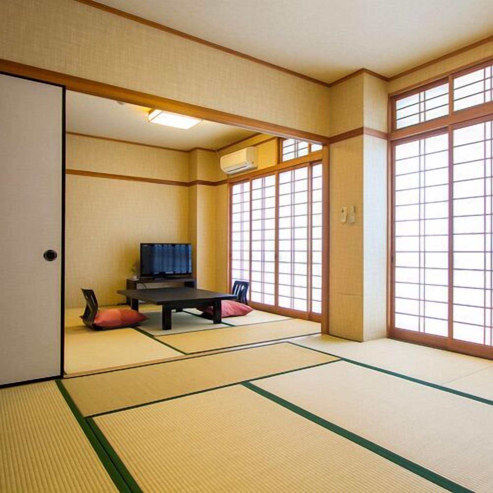 A traditional Japanese room with tatami flooring, a low table, a television, and sliding doors.