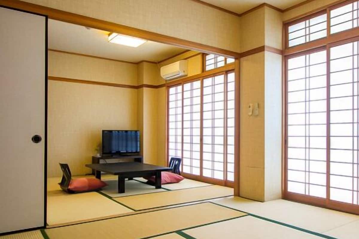 Una habitación japonesa tradicional con suelo de tatami, una mesa baja, un televisor y puertas correderas.