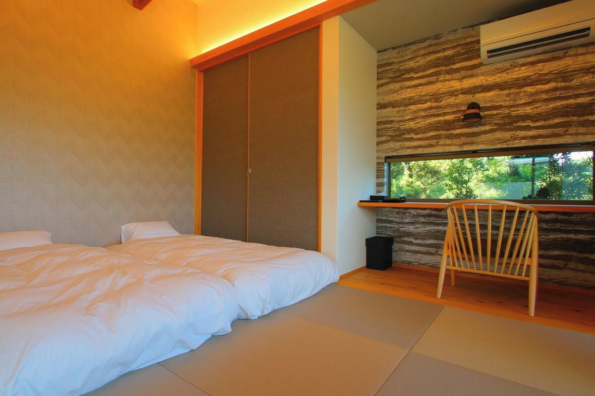 A bedroom with a bed, a chair, a window, and a wall with a textured pattern.