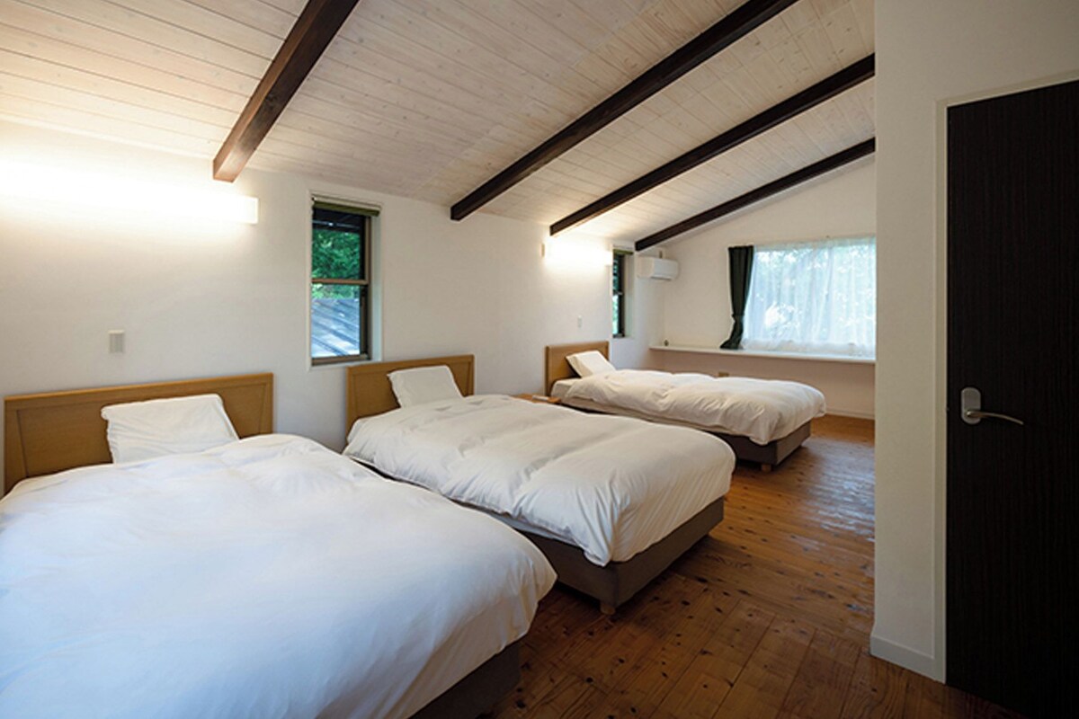 A room with three beds, wooden flooring, and a sloped ceiling with exposed beams.
