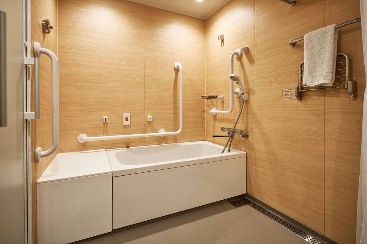 A modern bathroom with a bathtub, grab bars, and a towel rack.