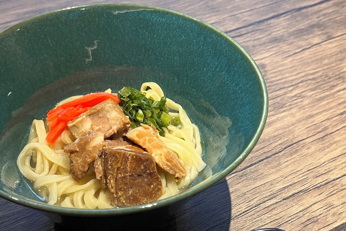 A bowl of noodles with meat and vegetables on a wooden table.