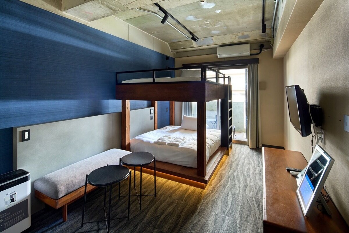 A bunk bed room with a desk, a small table, a TV, and a window.
