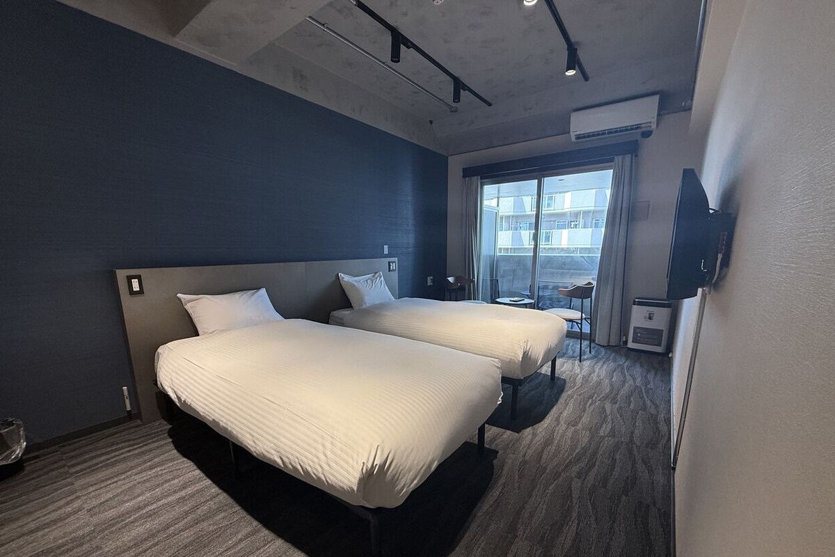 A hotel room with two beds, a TV, a small table, and a window with a view.