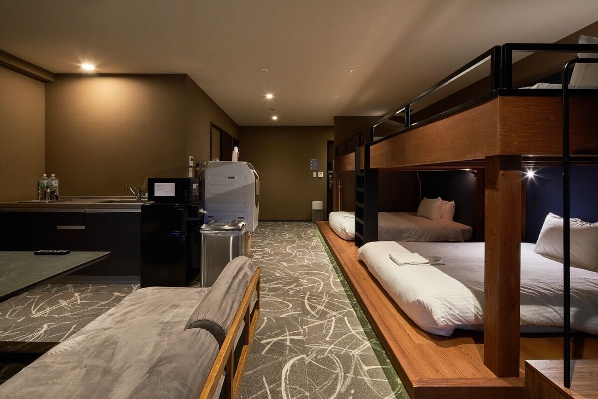 A hotel room with bunk beds, a desk, a sink, and a small kitchenette.