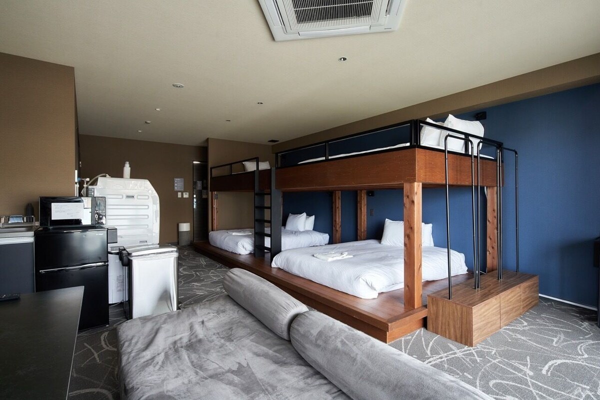 A hotel room with bunk beds, a kitchenette, and a seating area.