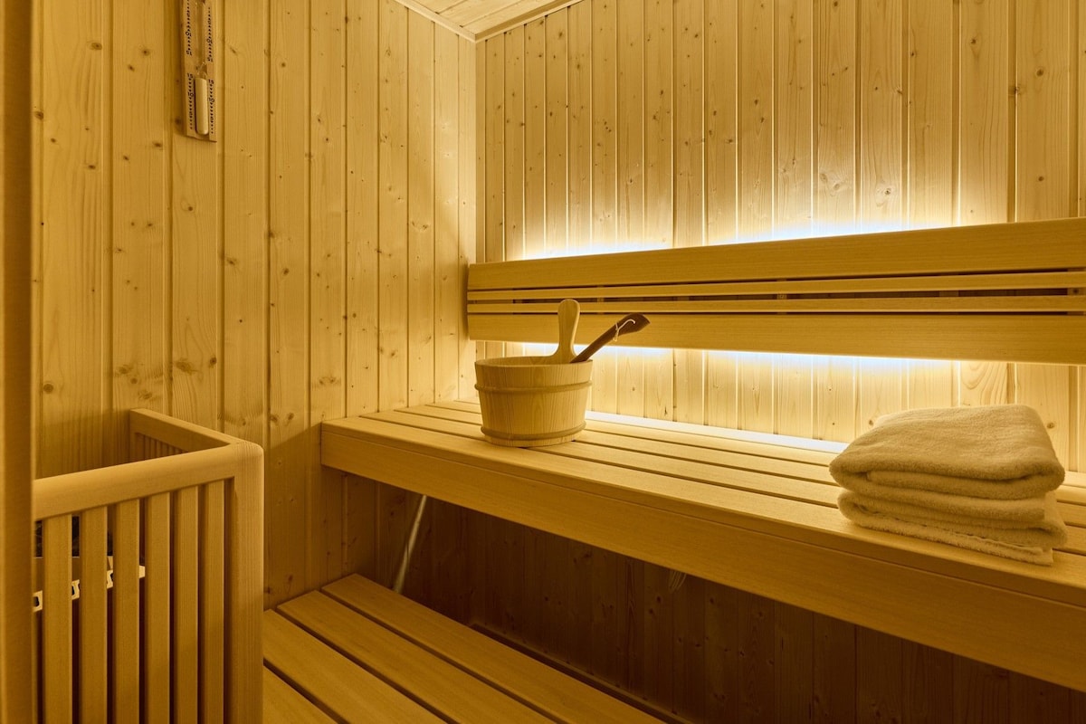 A wooden sauna with benches, a bench with a bucket and spoon, and a towel on the bench.