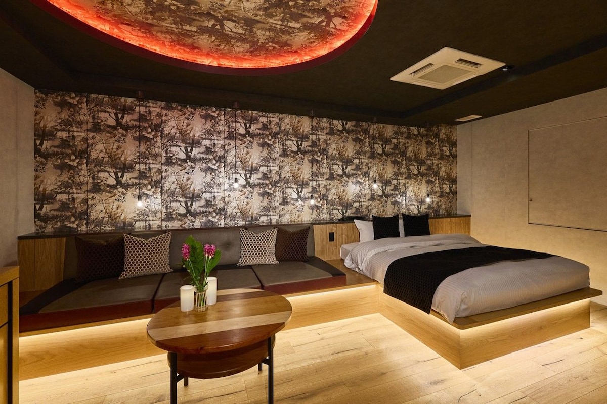 A modern bedroom with a bed, seating area, and a table with flowers.