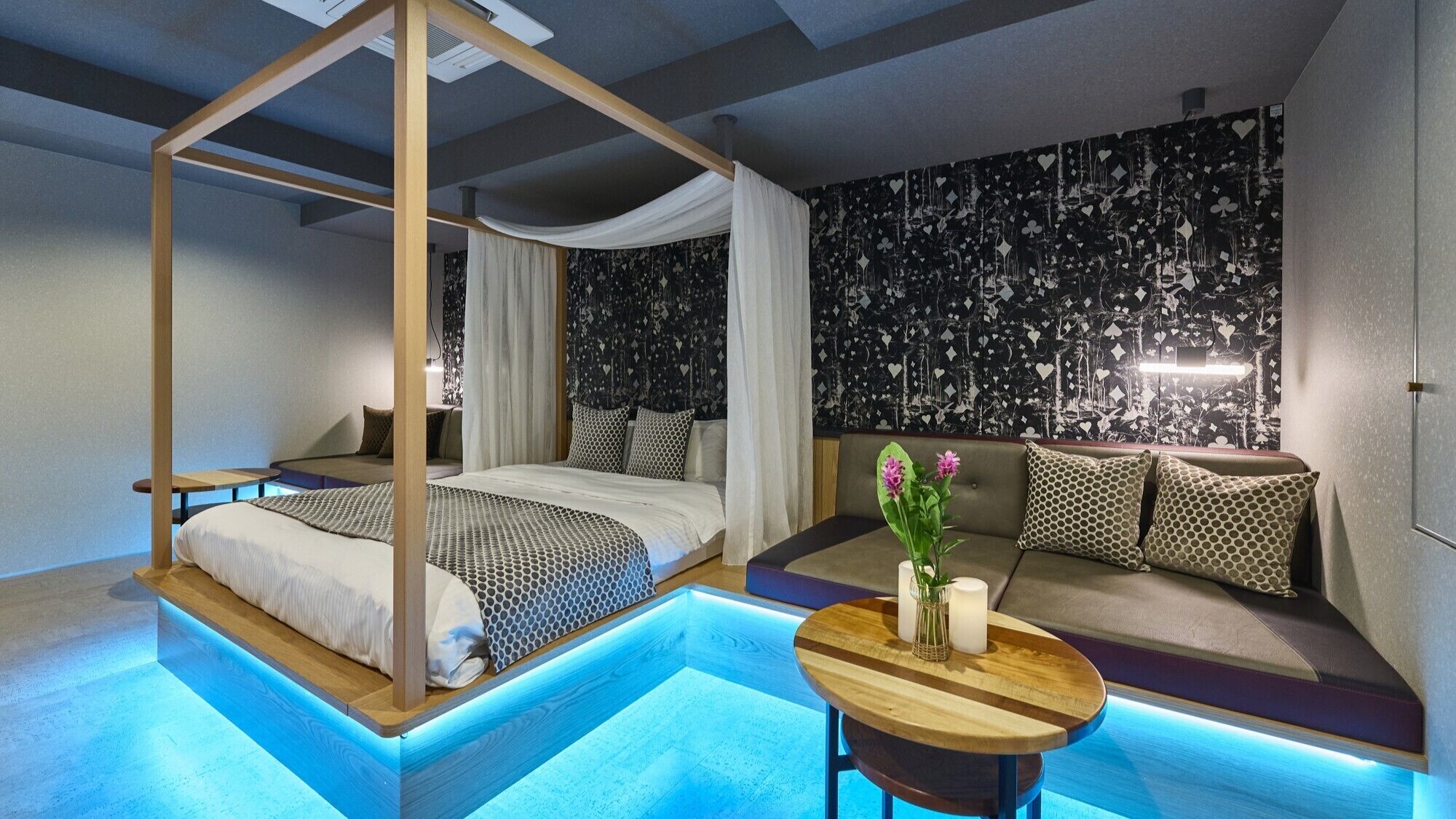 A modern bedroom with a canopy bed, a sofa, a small table with flowers, and a unique wall design.