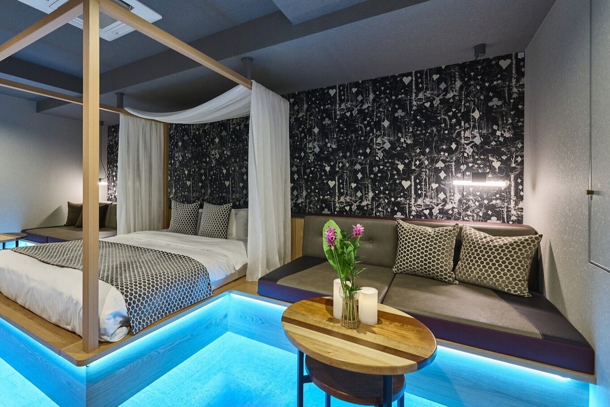 Un dormitorio moderno con cama con dosel, un sofá, una mesita con flores y un diseño de pared original.